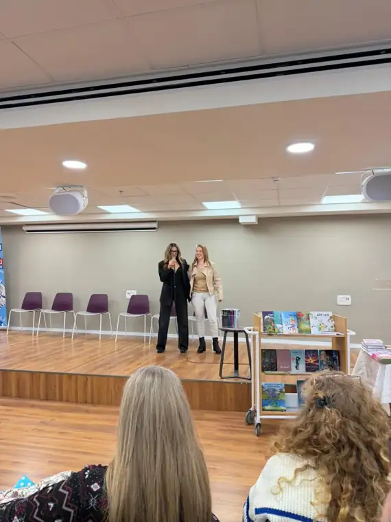 אורה אריאל במפגש עם קהל, לצד עגלת ספרים